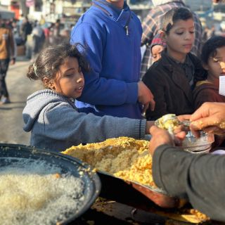 |طفلة فلسطينية تحاول الحصول على أقراص الفلافل الشعبية التي يتم إعدادها على نار الحطب، أمام خيم النازحين في...