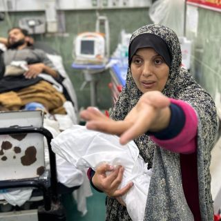 |الفلسطينية سوزان زعرب أثناء وداعها لأحفادها الطفلين وحملهم إلى والديهم المصابين في غرفة العمليات من أجل...